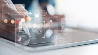 Es sind ein Laptop und Hände mit AI-Symbolen auf dem Foto zu sehen.